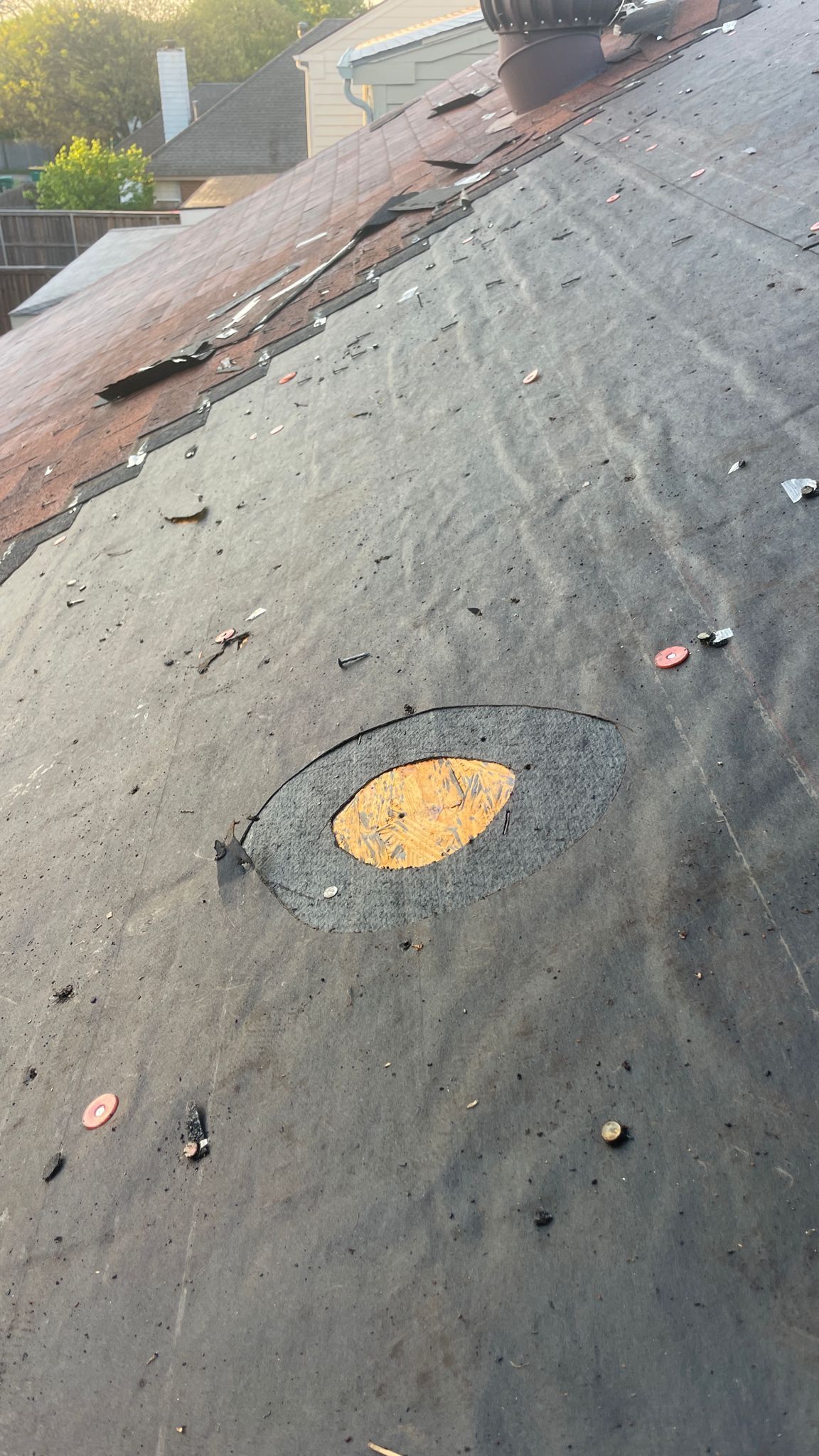 Close-up of a damaged flat roof with a circular hole. Black material with exposed yellow underlayment and debris.