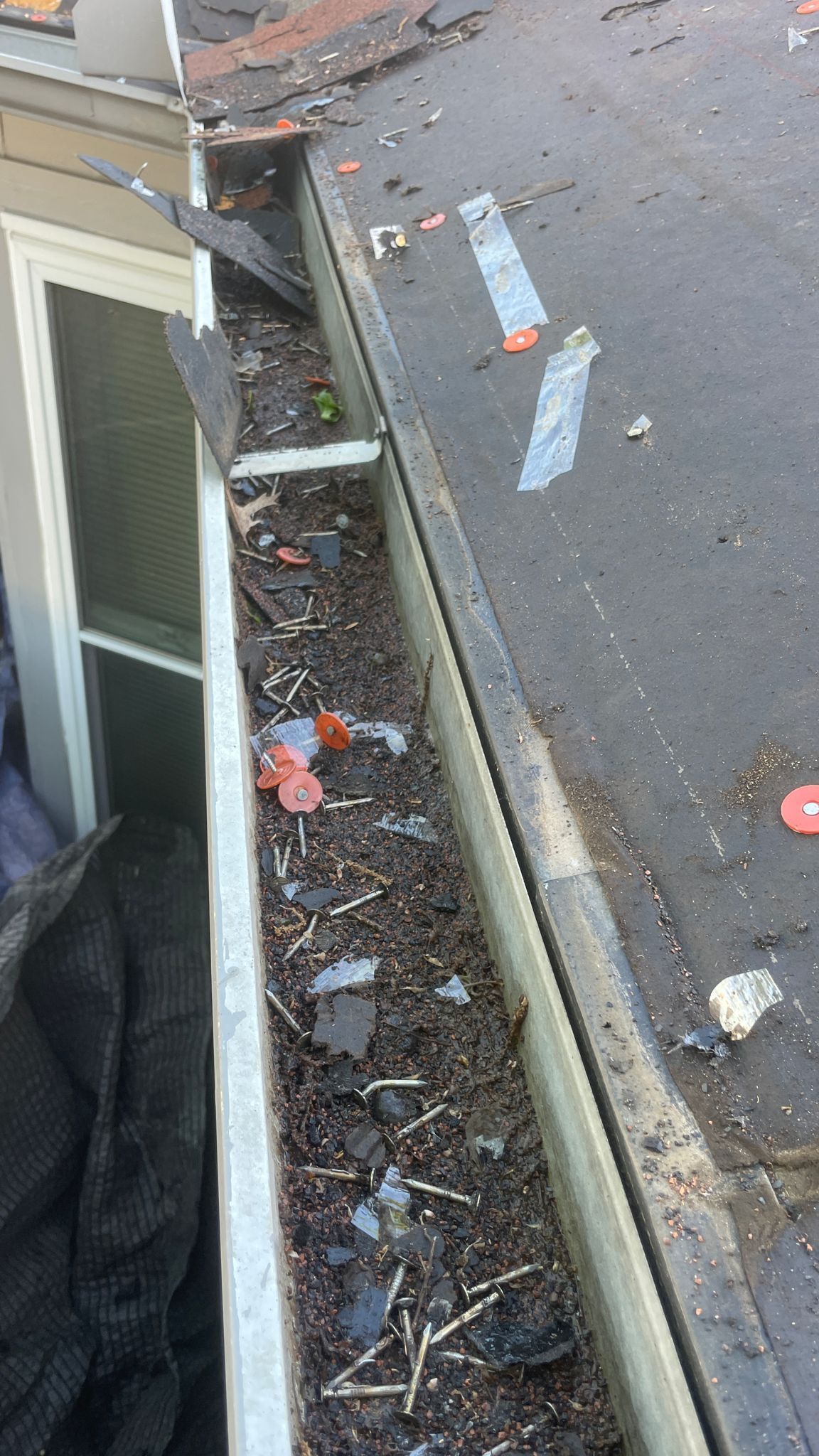 Gutter filled with debris on a roof. A window is visible on the left side.