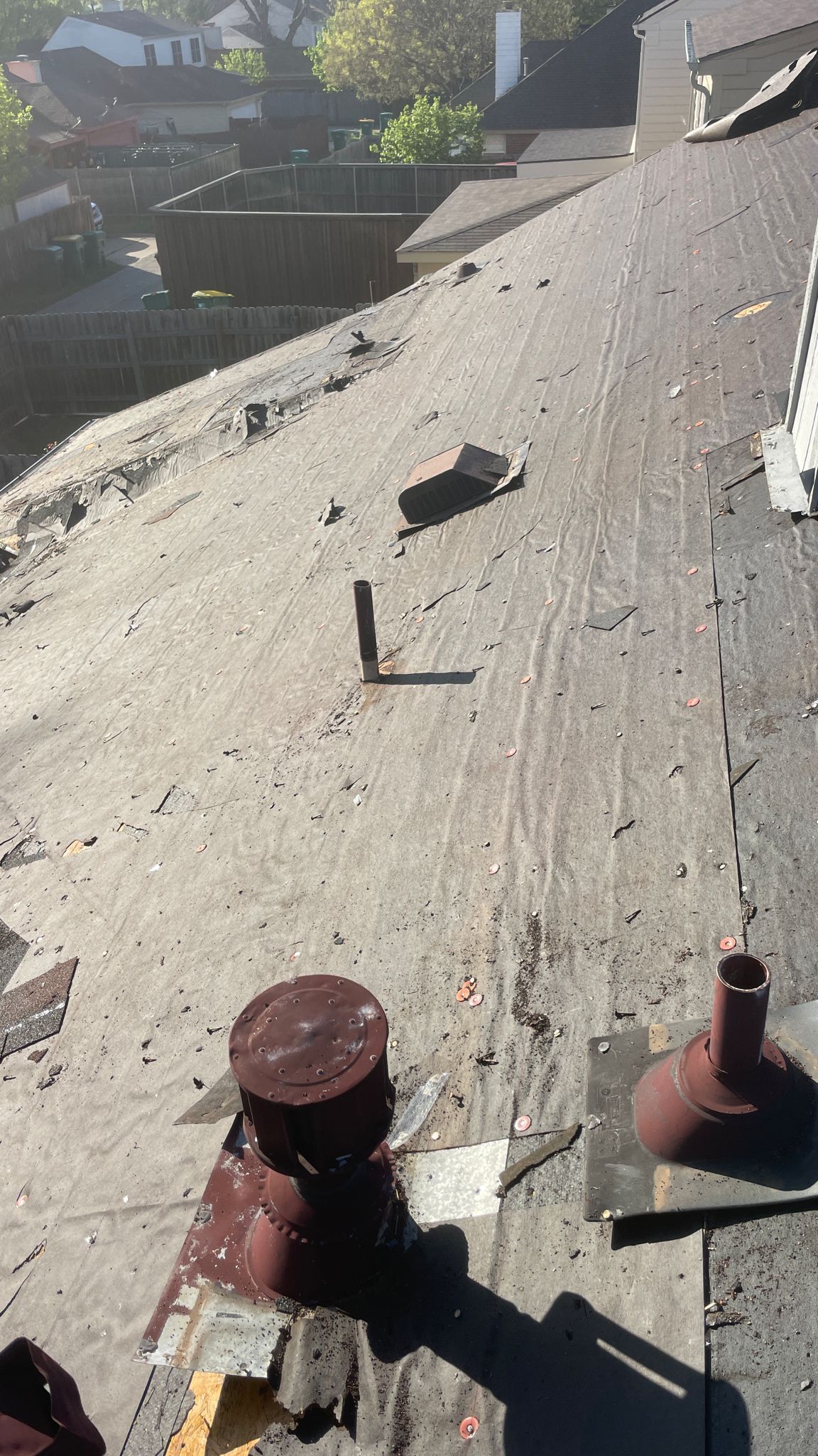 Damaged rooftop with debris and vents, overlooking a residential area on a sunny day.