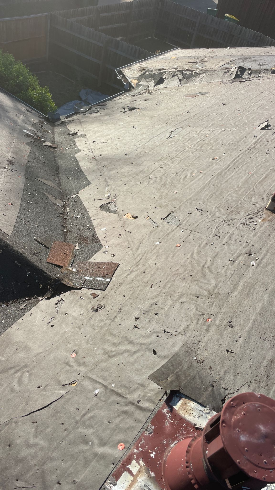 Rooftop view of a dark, flat surface with visible wear and tear, and a rusty cylindrical object in the foreground.