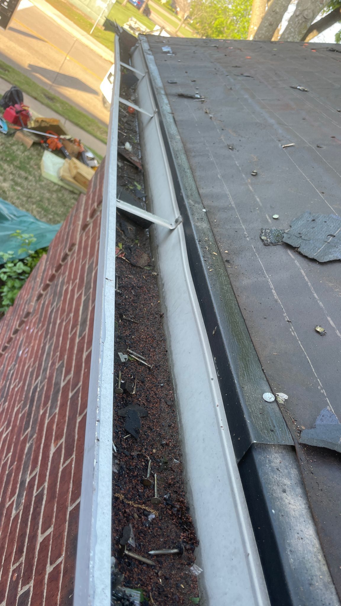 Gutter filled with debris on a roof next to a brick wall.