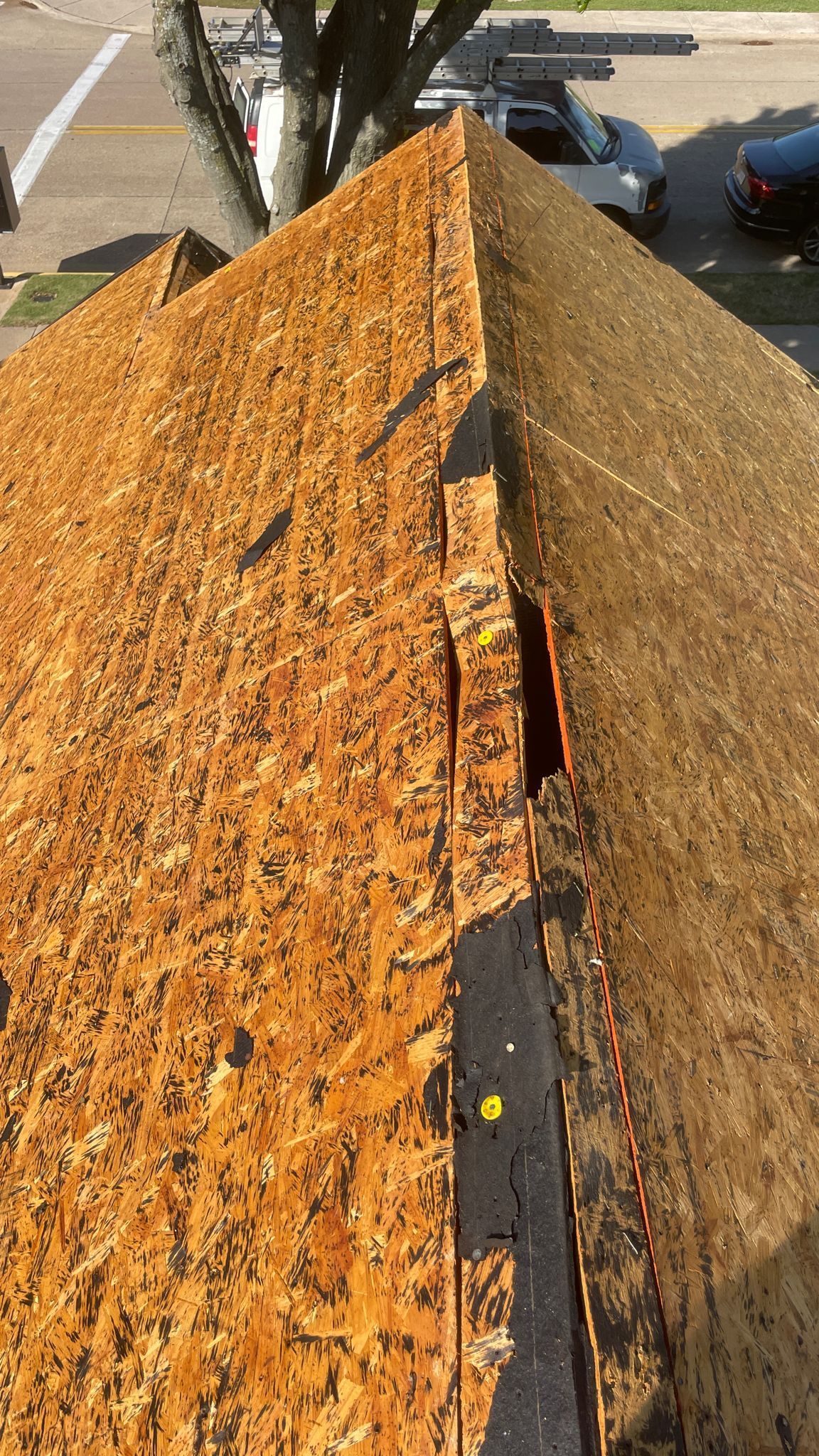 Overhead view of a roof’s edge with missing shingles, revealing the wooden structure and underlying felt.