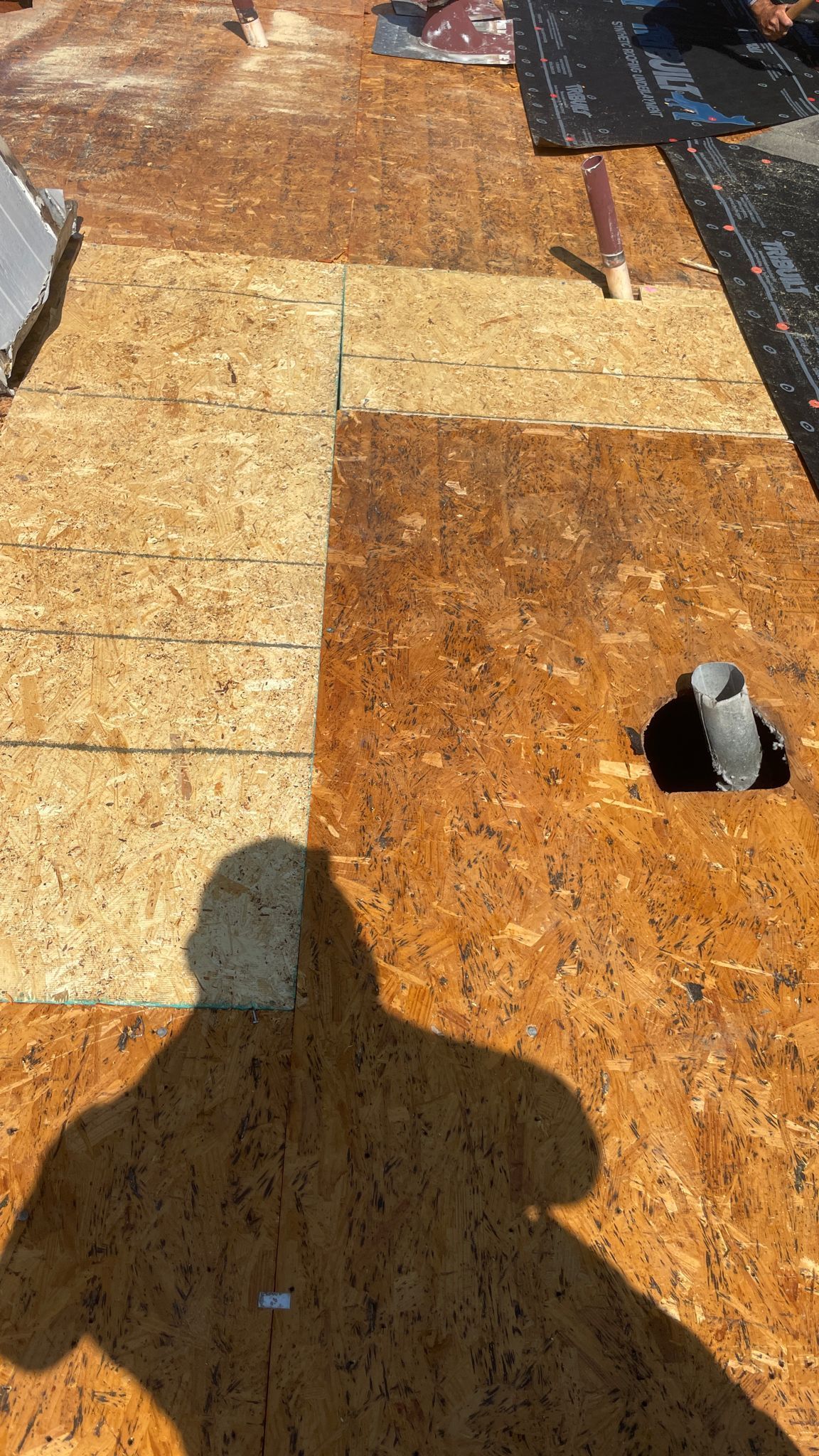 A damaged roof with exposed wood panels, a vent pipe, and a partially covered hole.