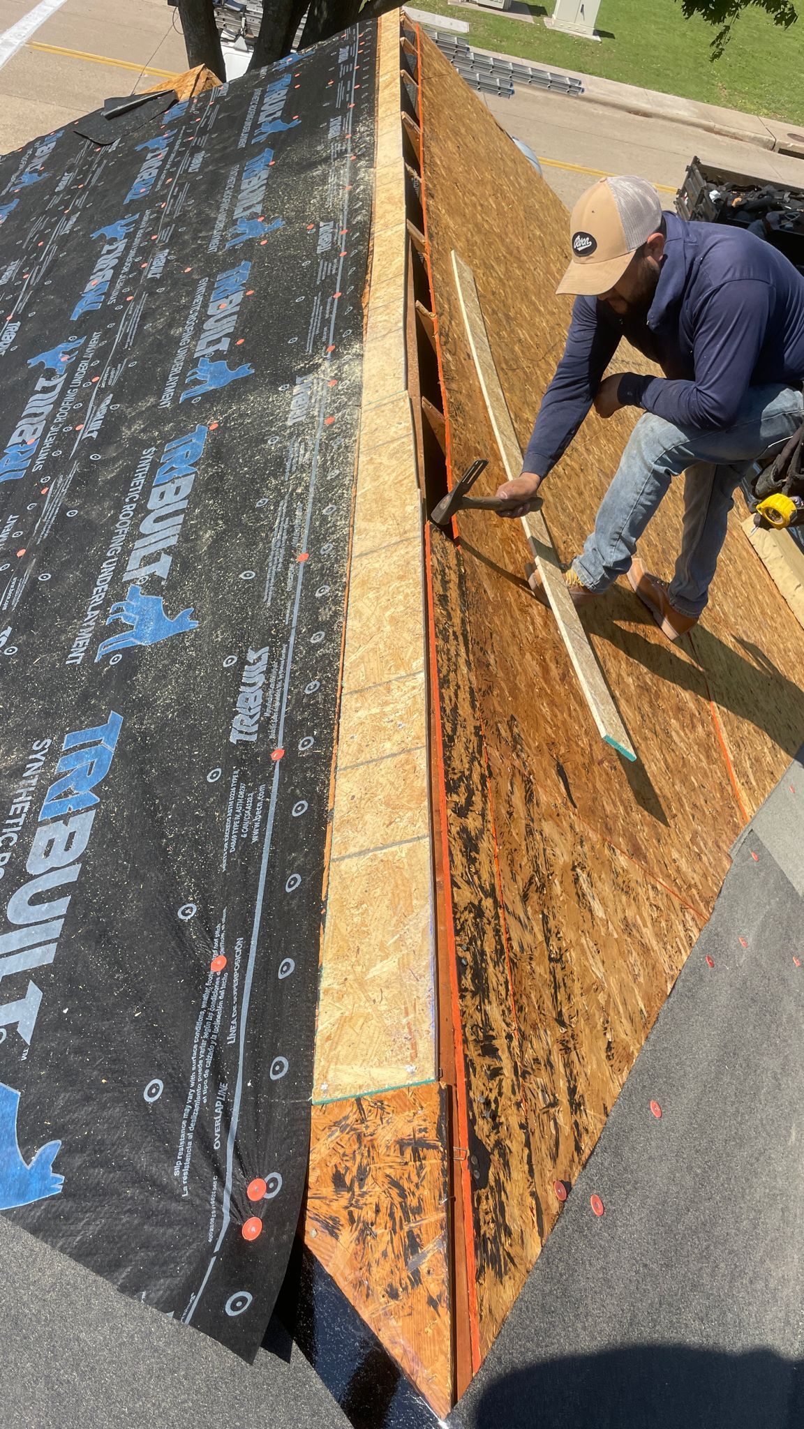Roofer working on a roof, installing materials. Boards, underlayment, and a person holding a tool are visible.