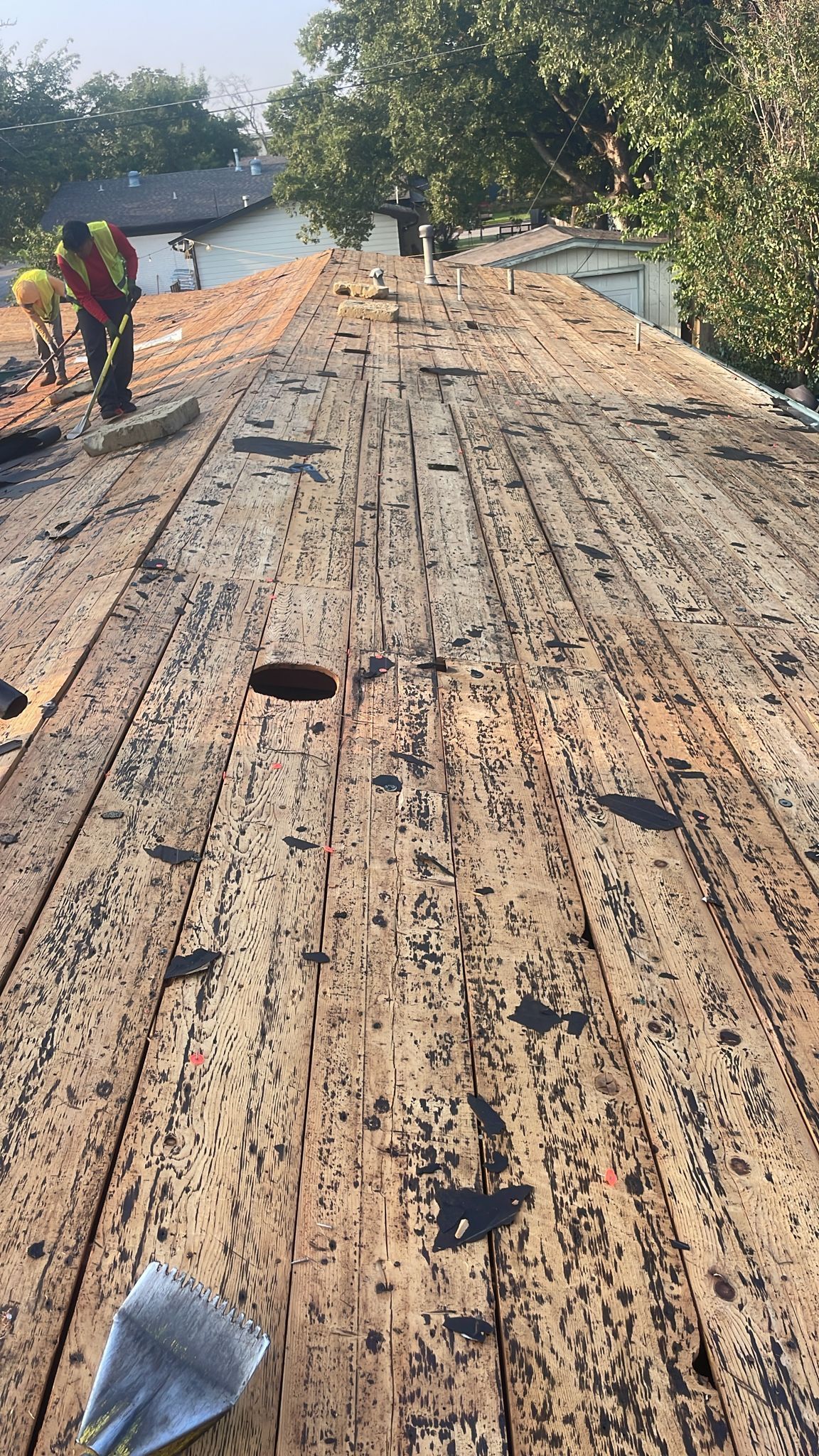Workers removing old roofing materials from a weathered wooden roof.