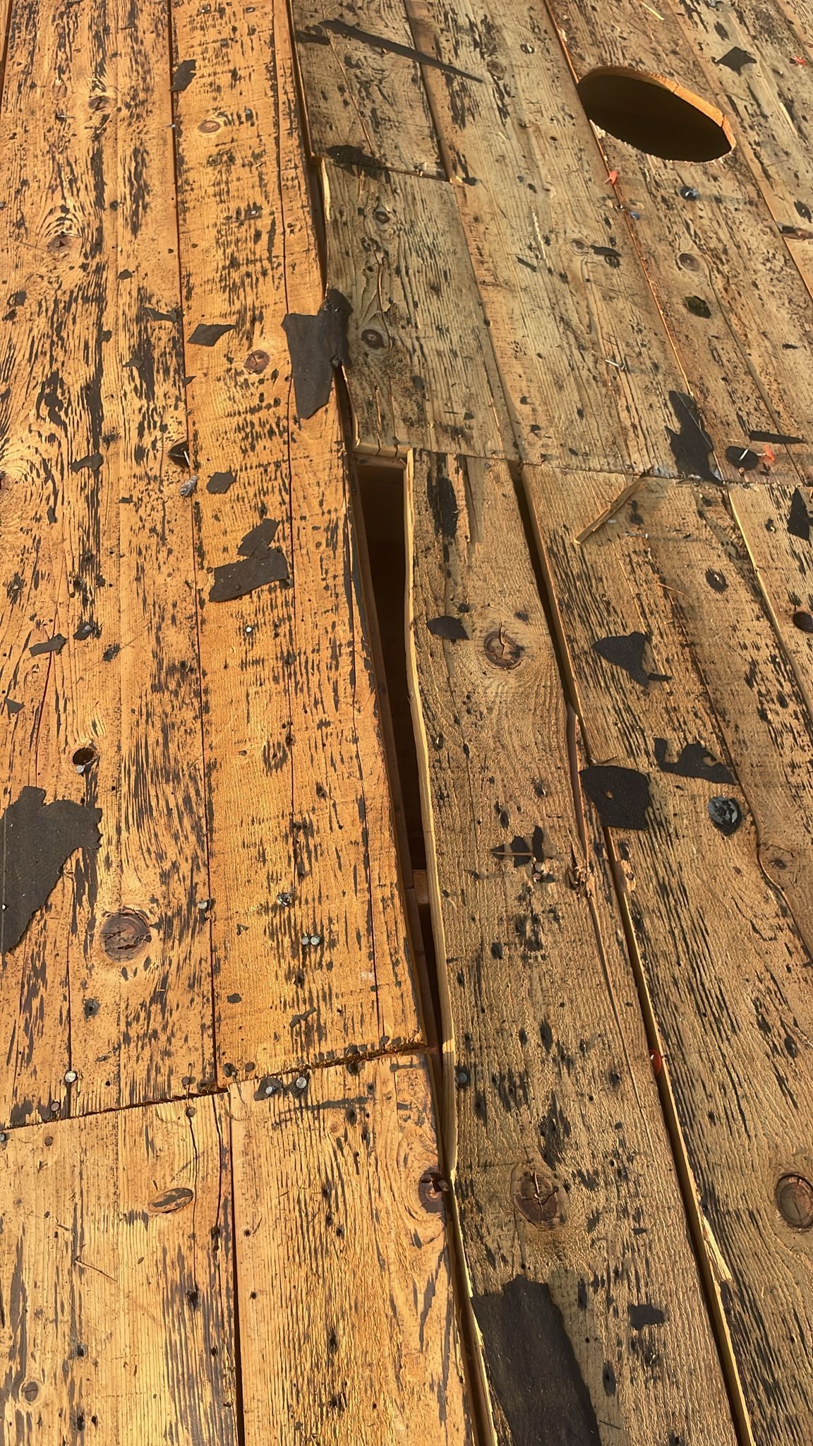 Close-up of weathered wooden planks with a large gap between them and a circular hole.