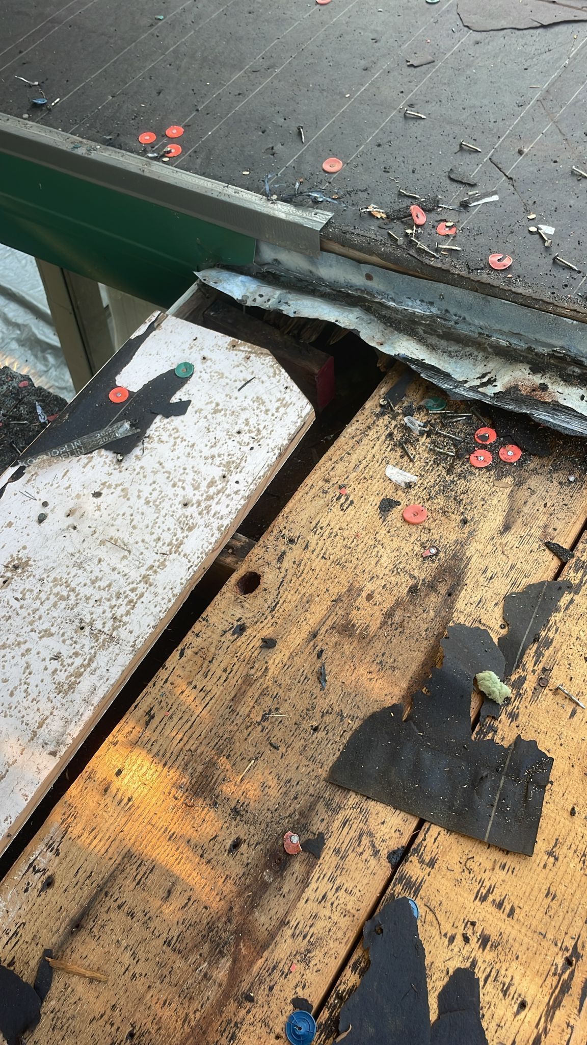 Close-up of damaged roof edge; exposed wood, metal flashing, and scattered roofing debris.