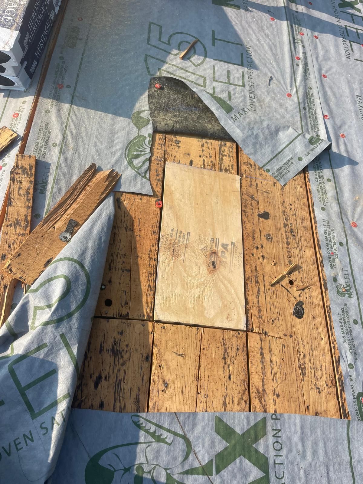 Roofing materials: wooden planks, plywood, blue underlayment, nails, and a partially covered area.