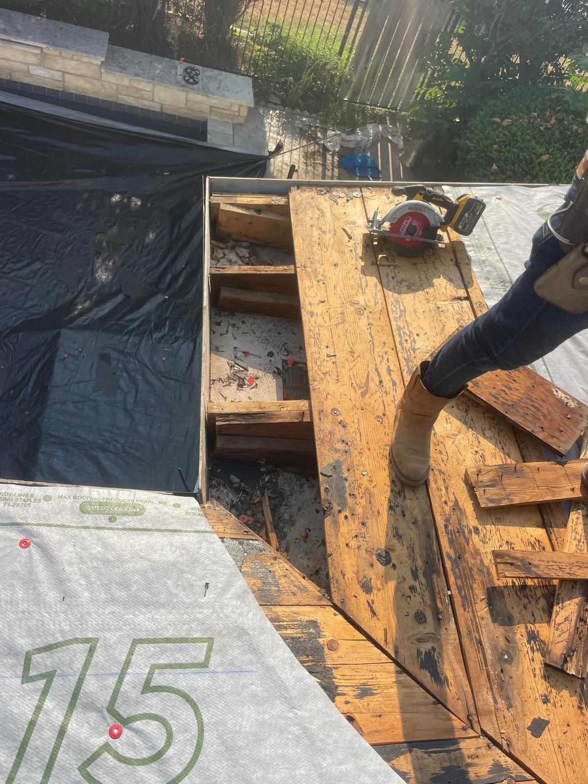 Roofer using a saw on a slanted roof; debris and tarp are visible. Sunlight.