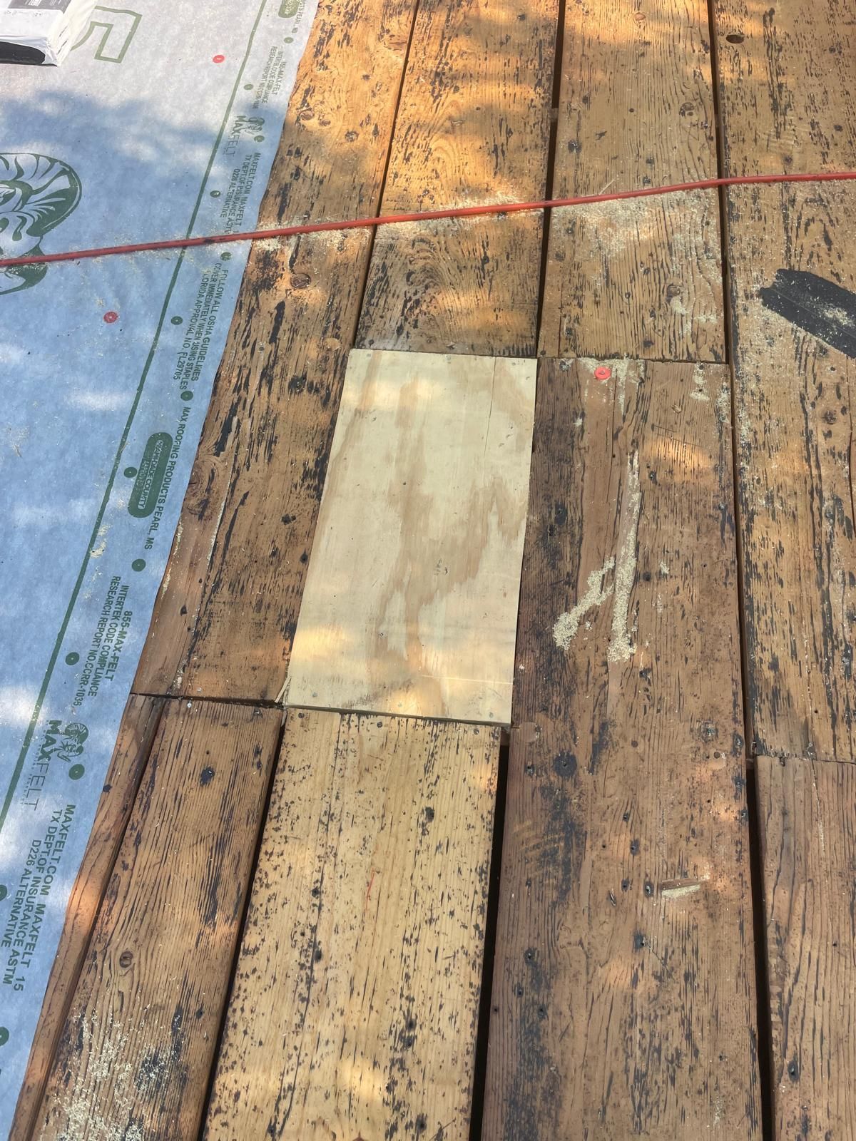 Wooden roof with a plywood patch; roofing paper partially visible.