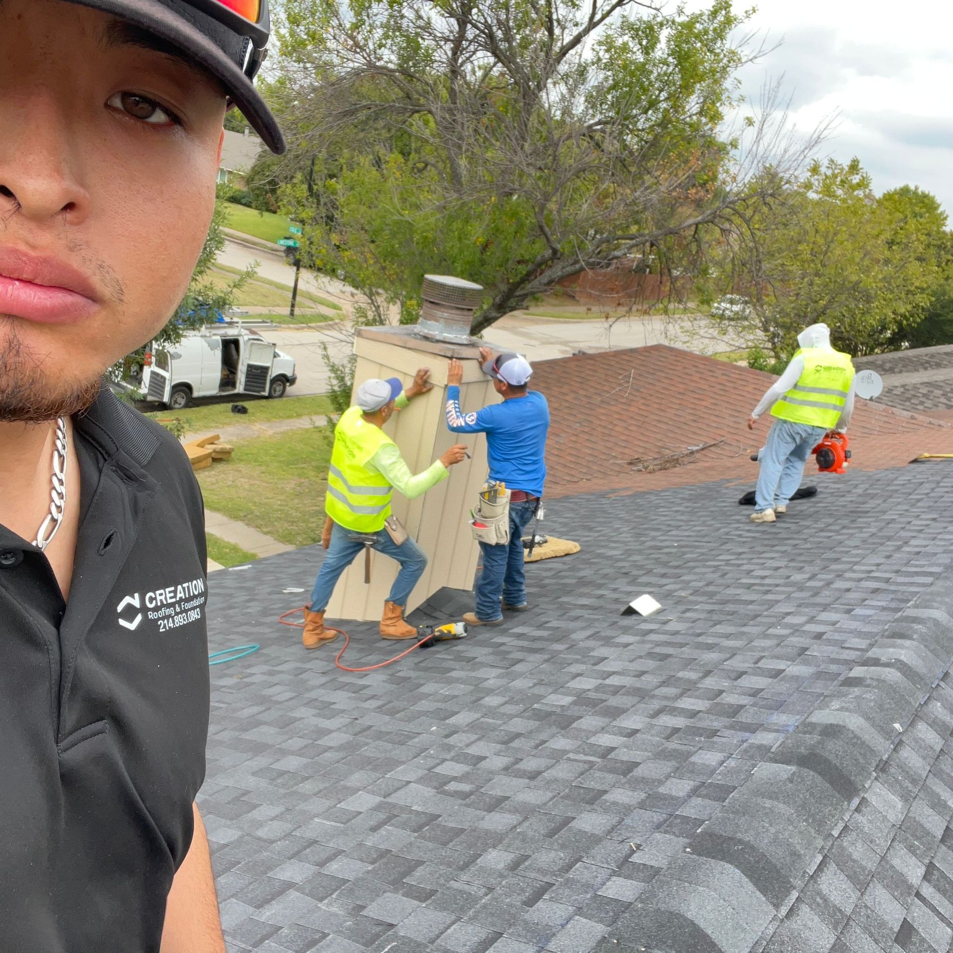 Man taking selfie with three roofers working on a roof; wearing safety vests.