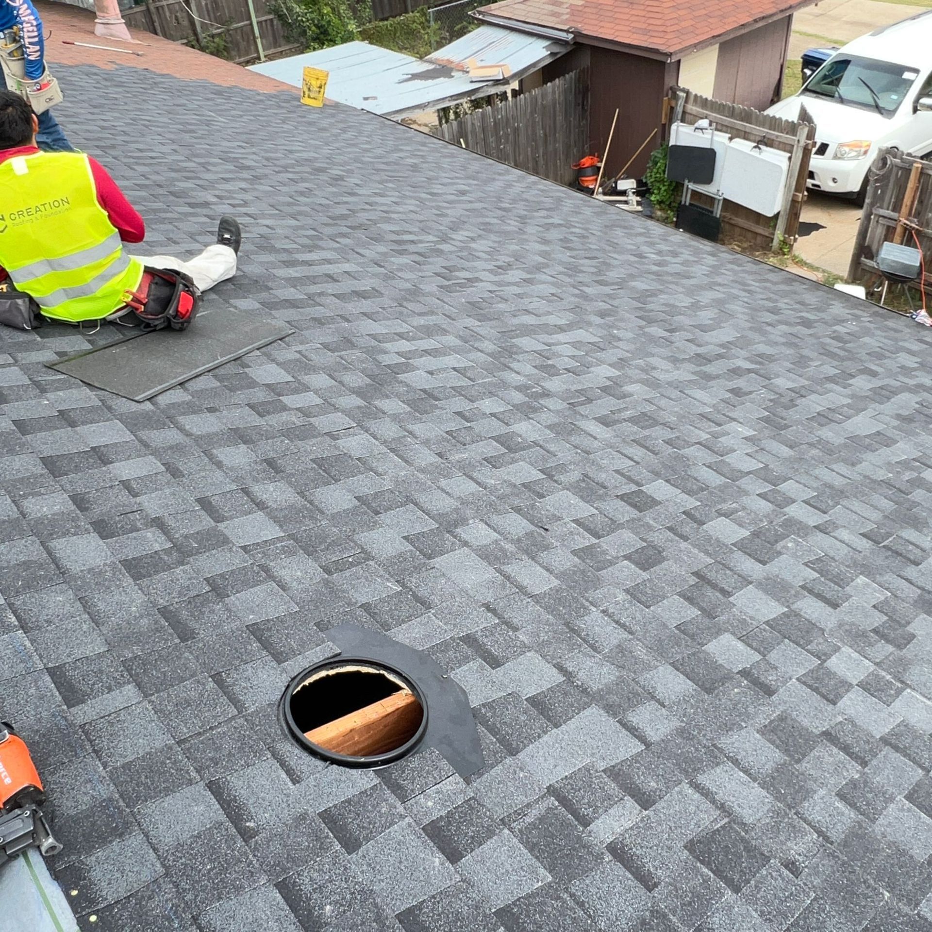Person on a gray shingle roof, near an open vent and tools.