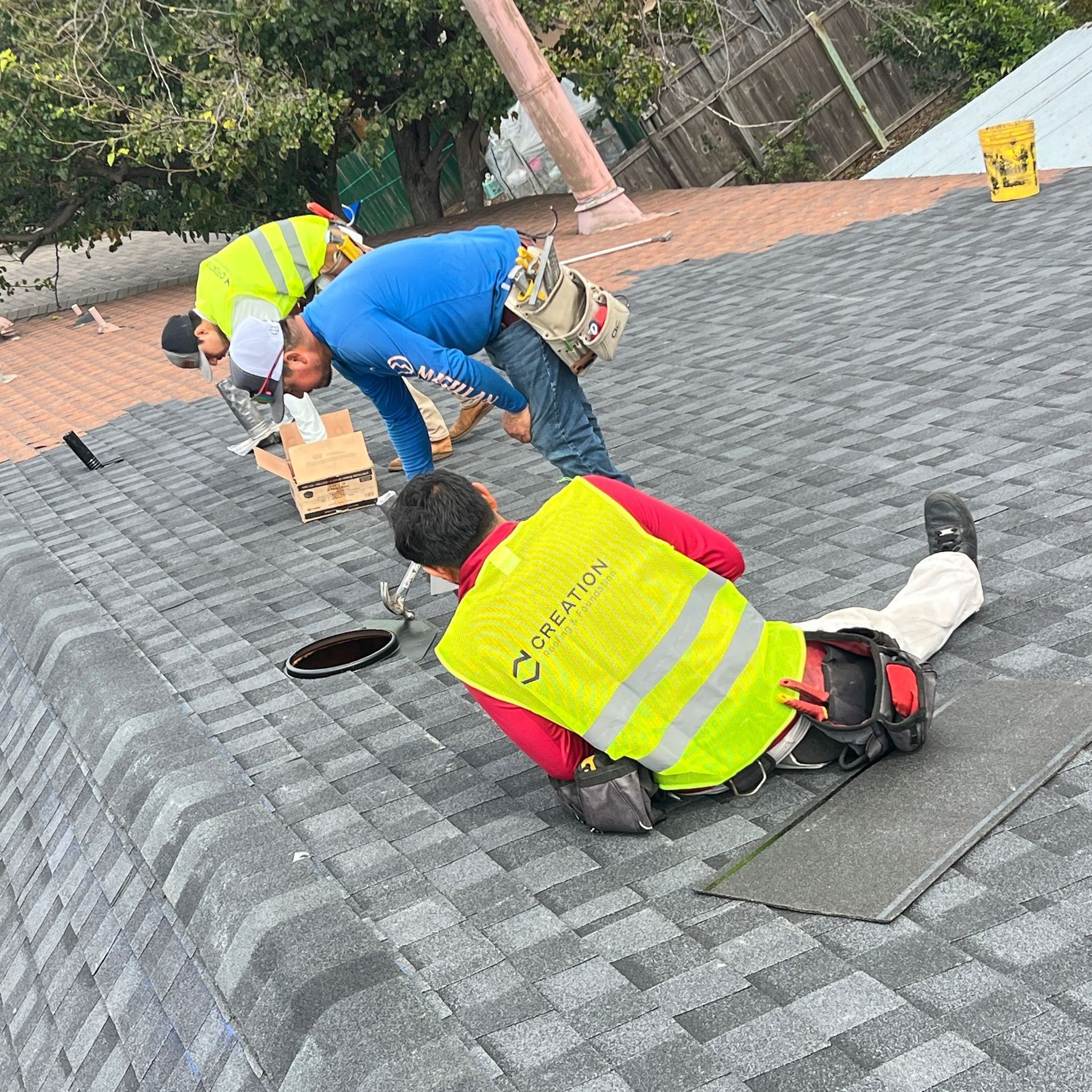 Roofers installing shingles on a roof, wearing safety vests.
