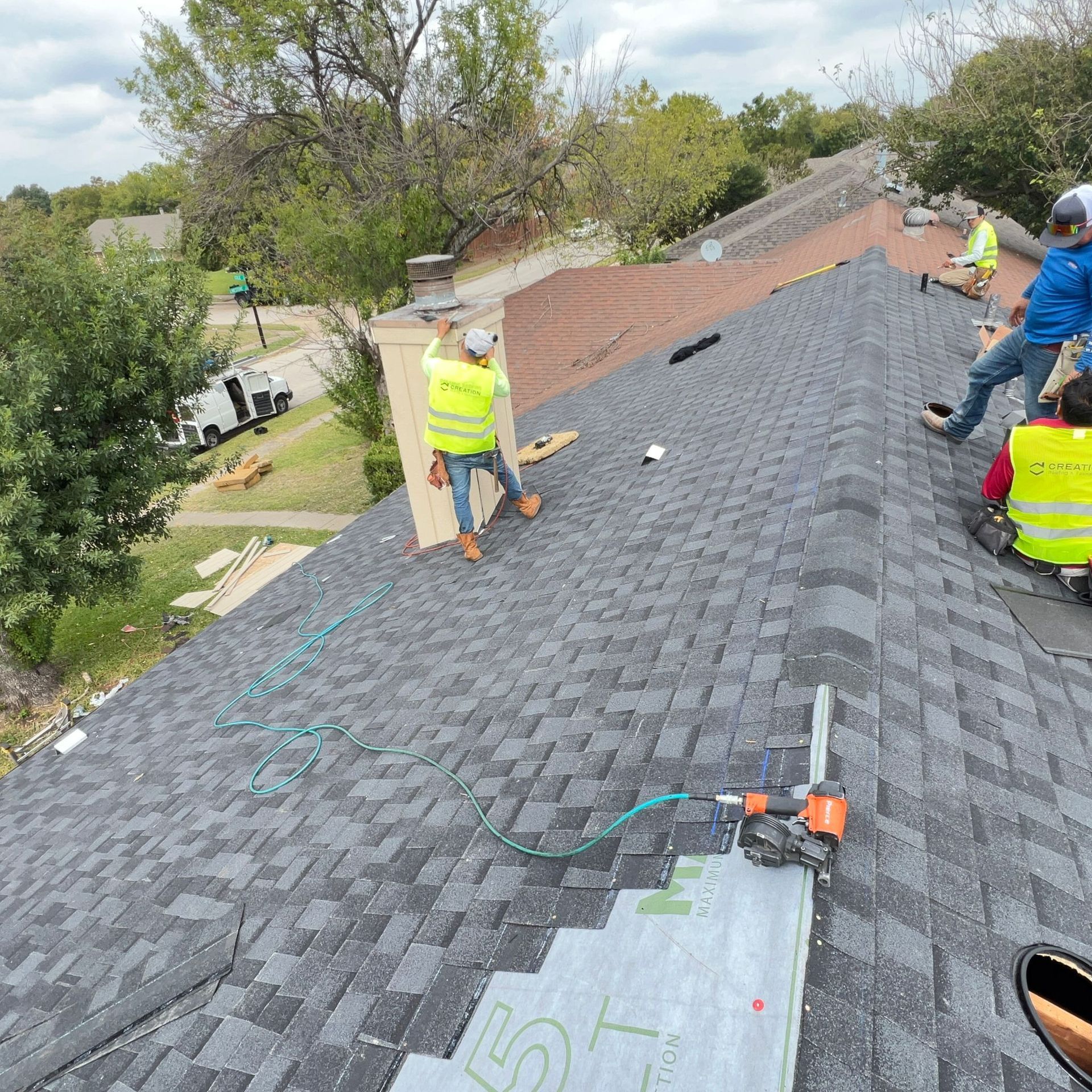 Roofers installing shingles on a roof, wearing safety vests.