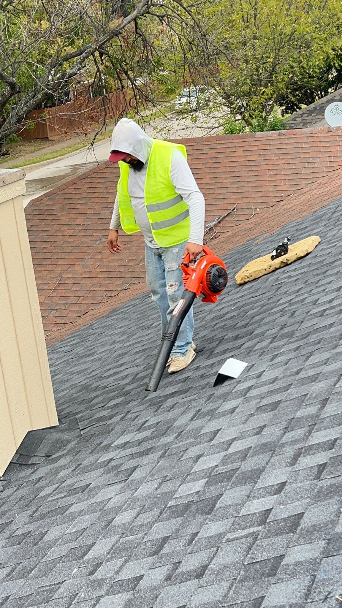 Person on a roof blowing debris. They wear a safety vest and hoodie.