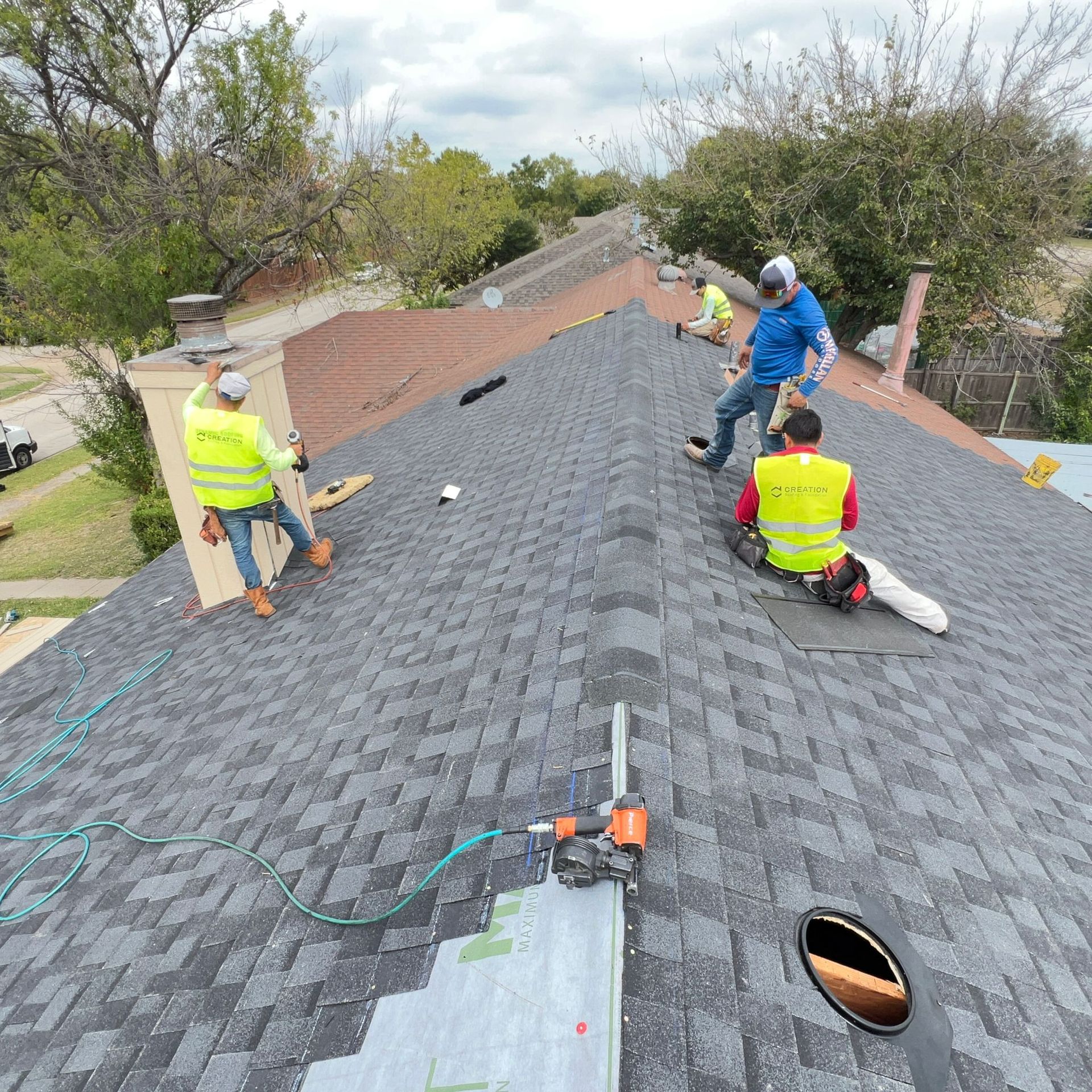 Roofers working on a house roof. One is using a saw. Others wear safety vests.