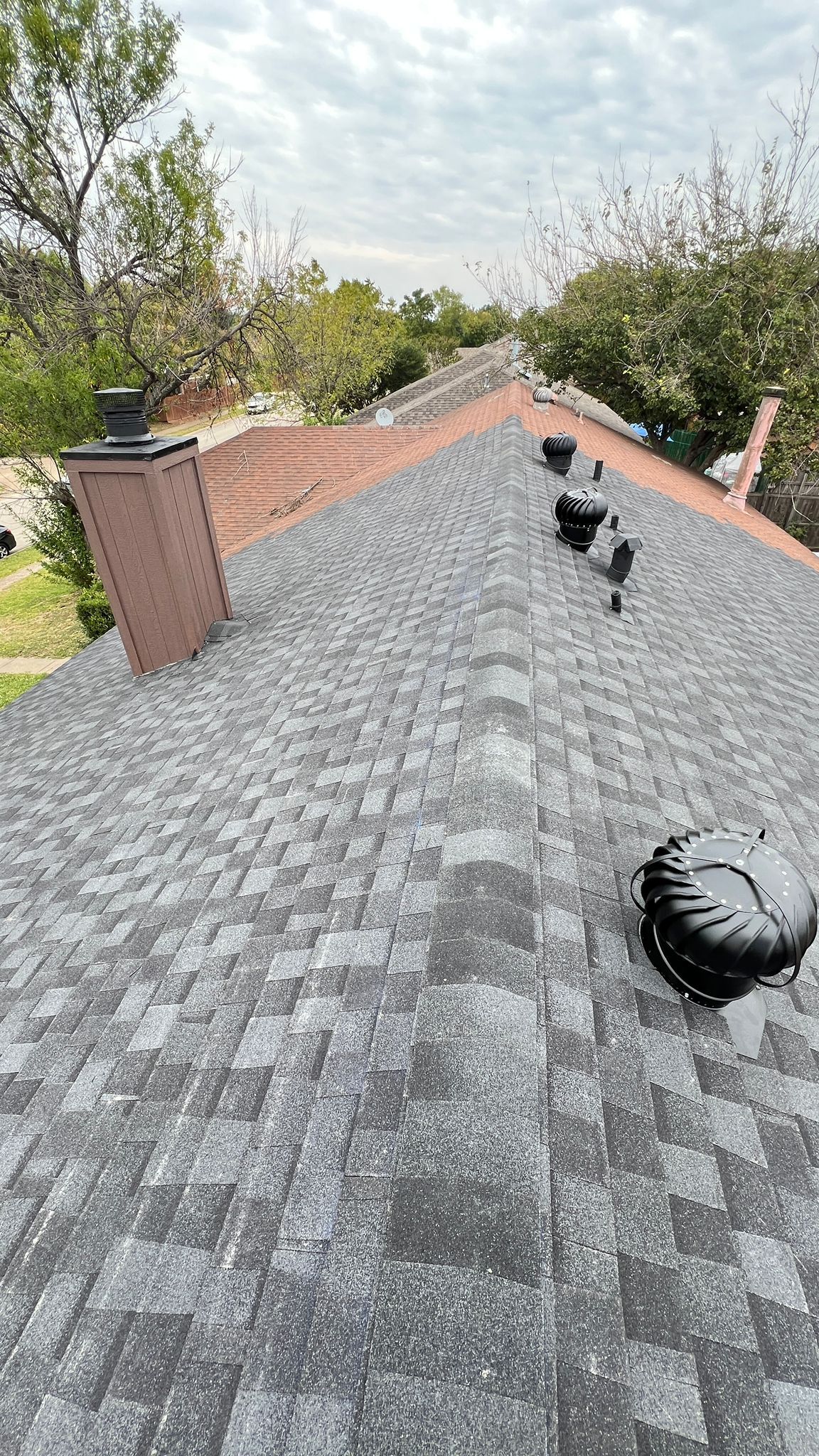 Gray shingle roof with vents and a brick chimney under a cloudy sky.