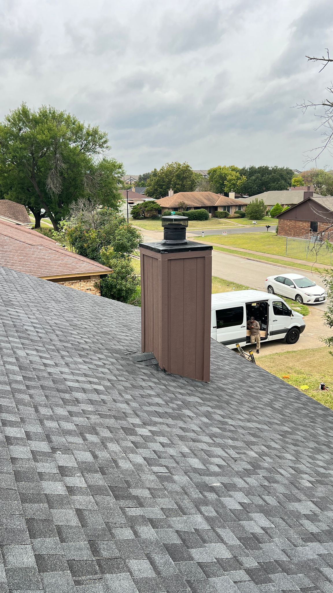 Brown chimney on a gray shingled roof with a green cap, cloudy sky.