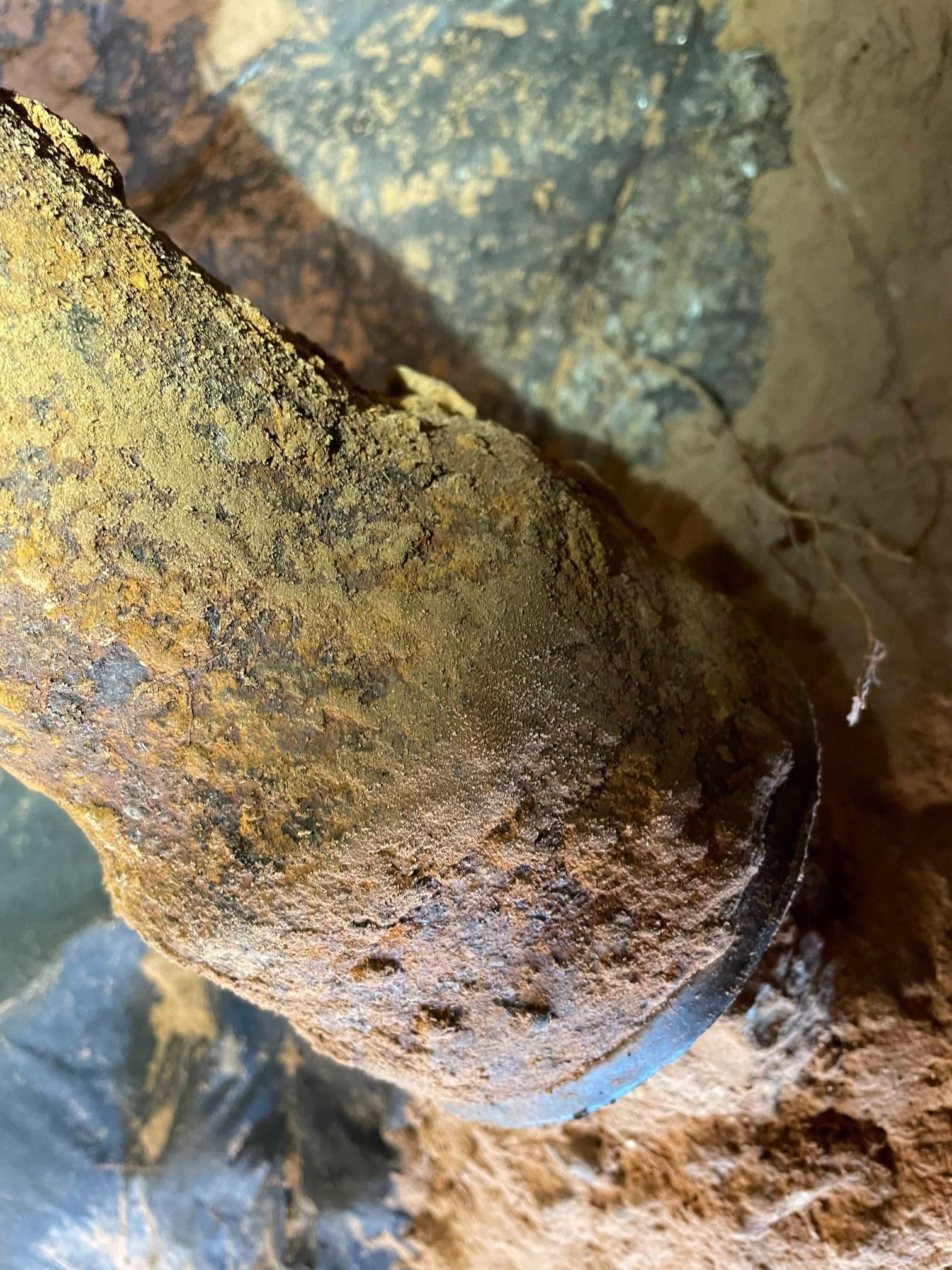 Rusty, metal pipe resting on rocky surface with dark shadows and various textures.
