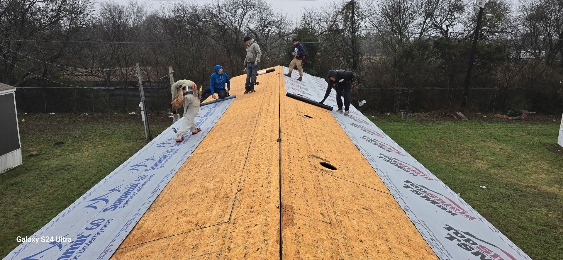 Roofers installing roofing material on a house, overcast day.