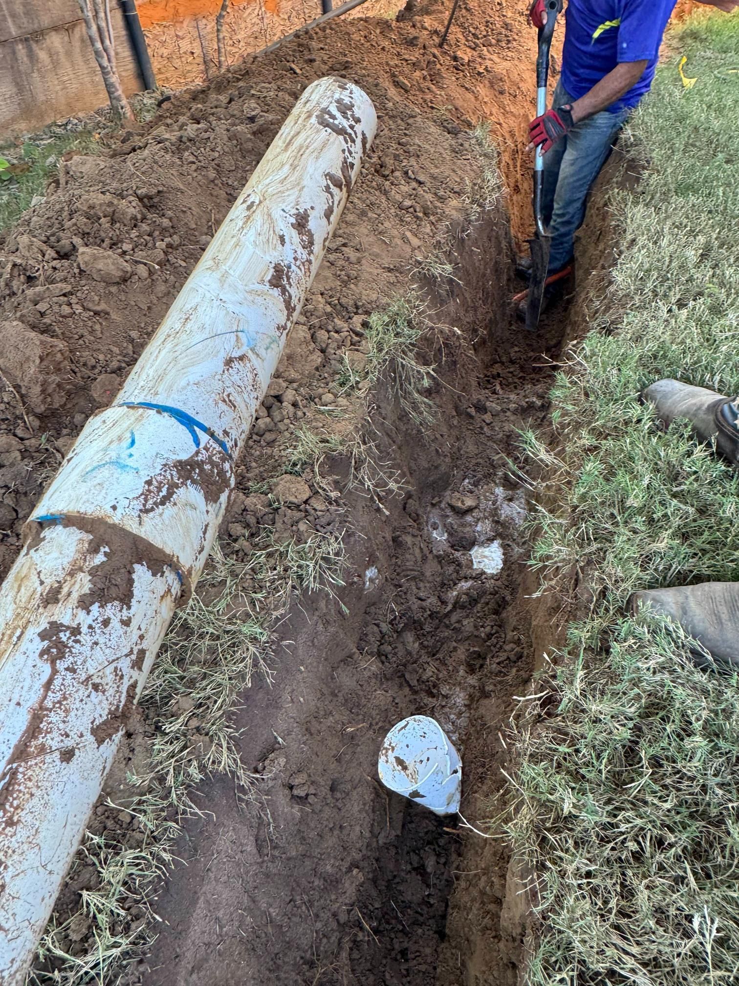 Person digging a trench next to a large white pipe.