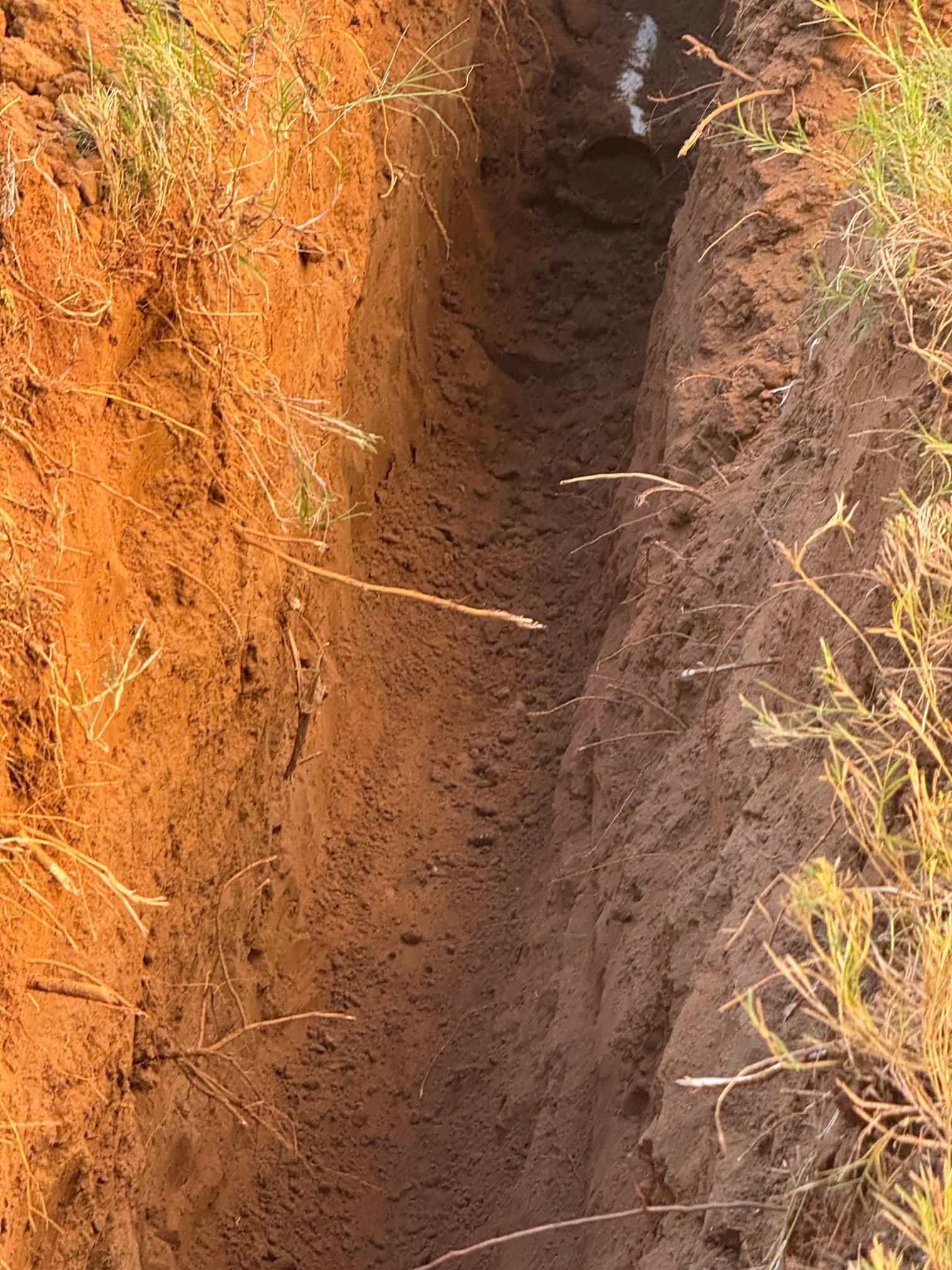 Narrow trench dug in reddish-brown earth, with grass along the edges.