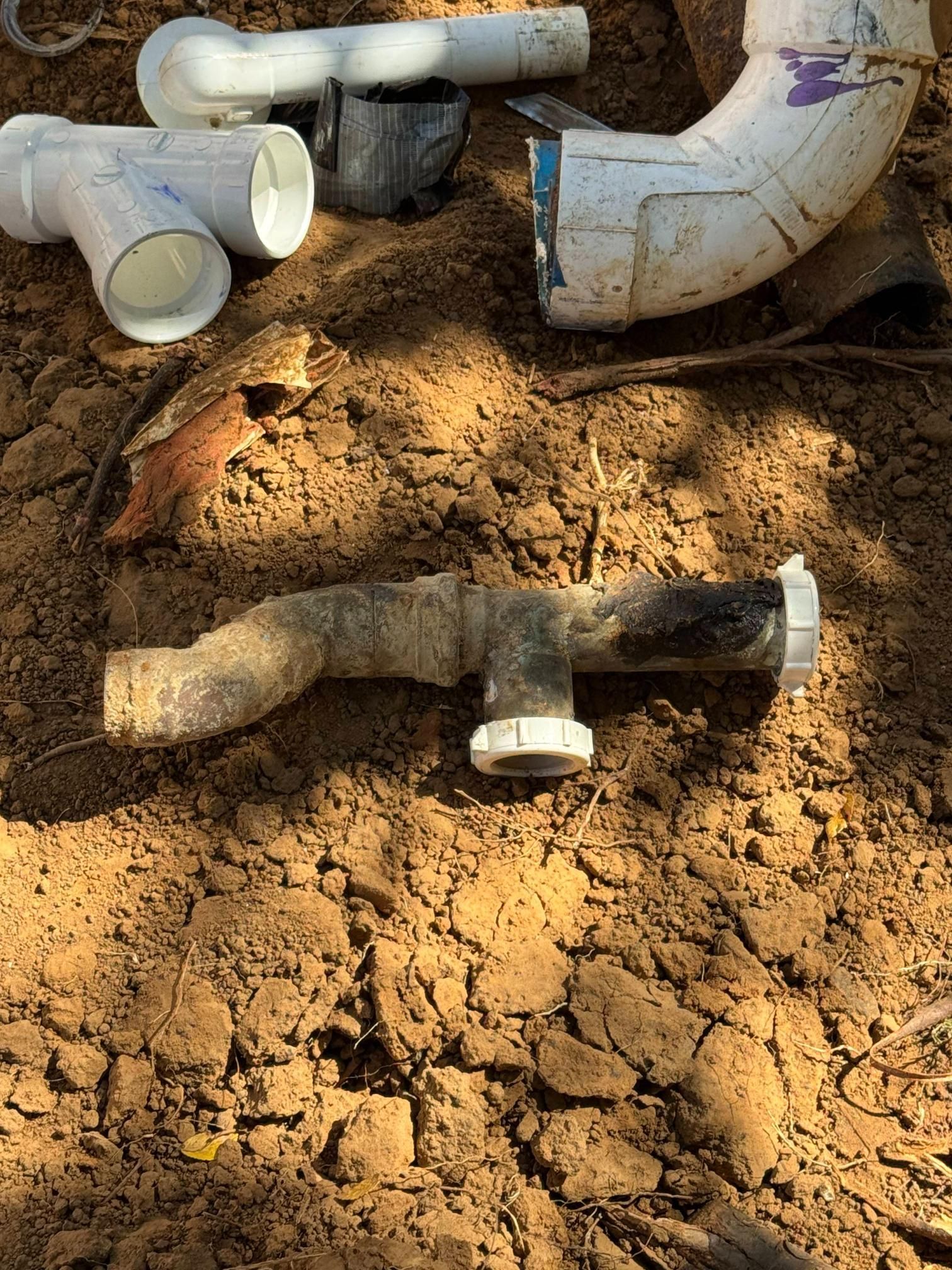 Plumbing pipes and fittings in dirt, possibly for repair or installation. White and black plastic.