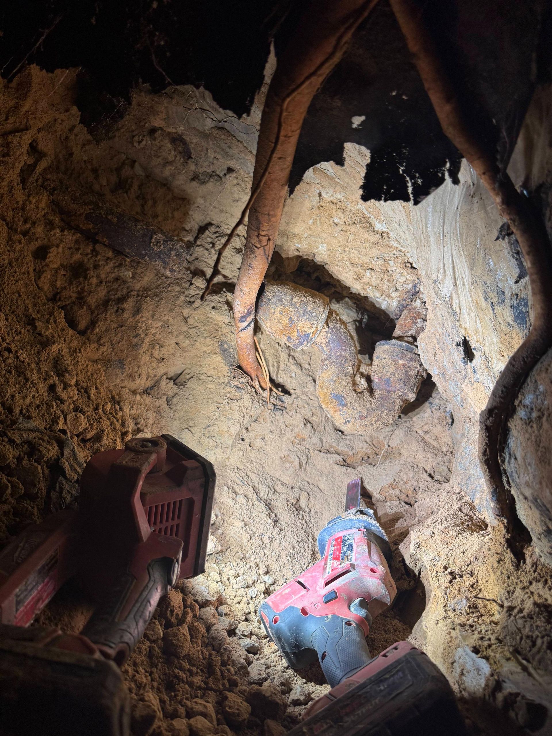 Roots and tools in an underground tunnel. A red drill is near a pile of sand.