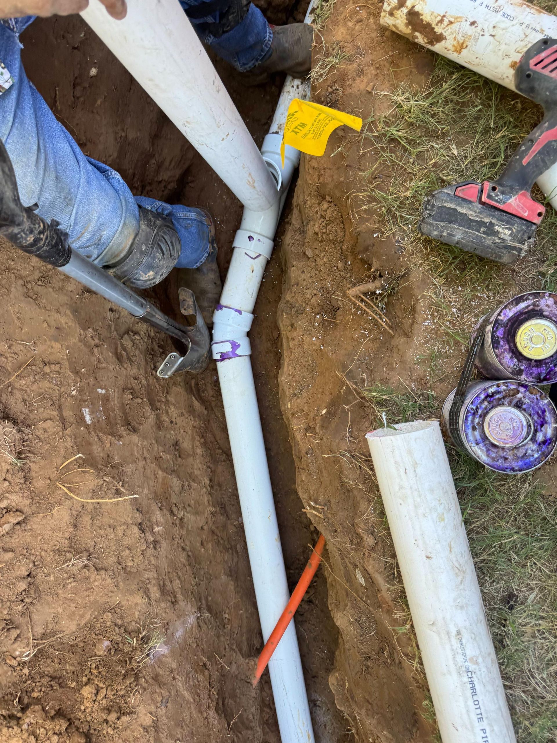 PVC pipes being installed in a trench; person working with tools.