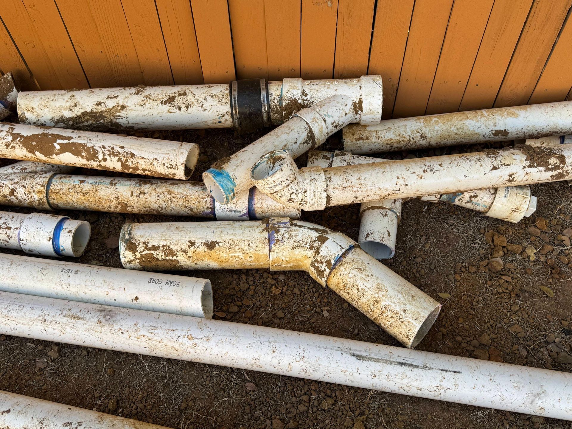White PVC pipes and fittings scattered on the ground near an orange wooden wall.