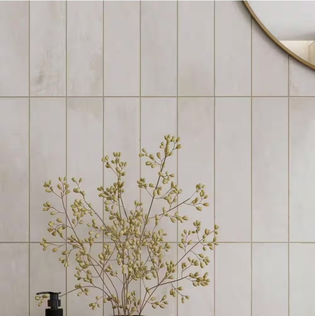 Vertical cream-colored tiles with light-colored grout, a vase of branches, and a circular mirror.
