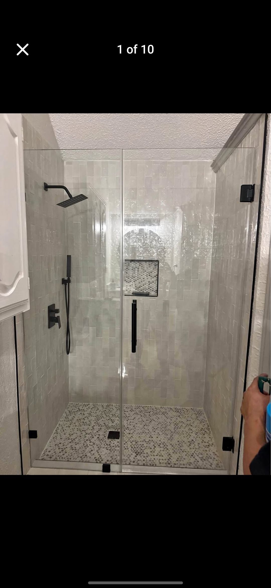 A modern shower with clear glass doors and black fixtures. The floor is covered with small stones.
