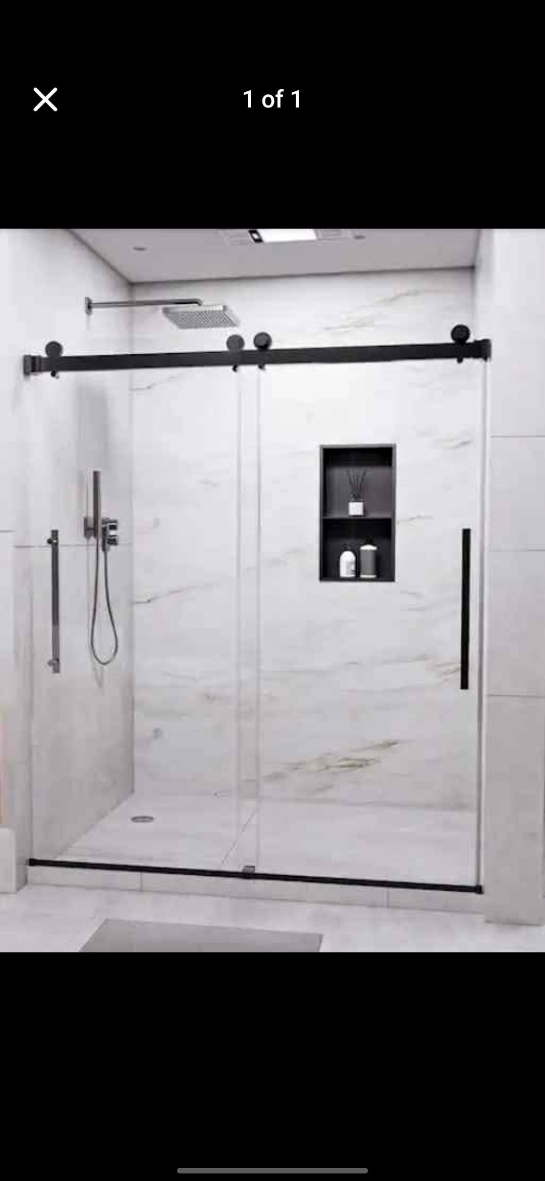 A modern shower with a sliding glass door and black hardware. White marble tiles cover the walls.
