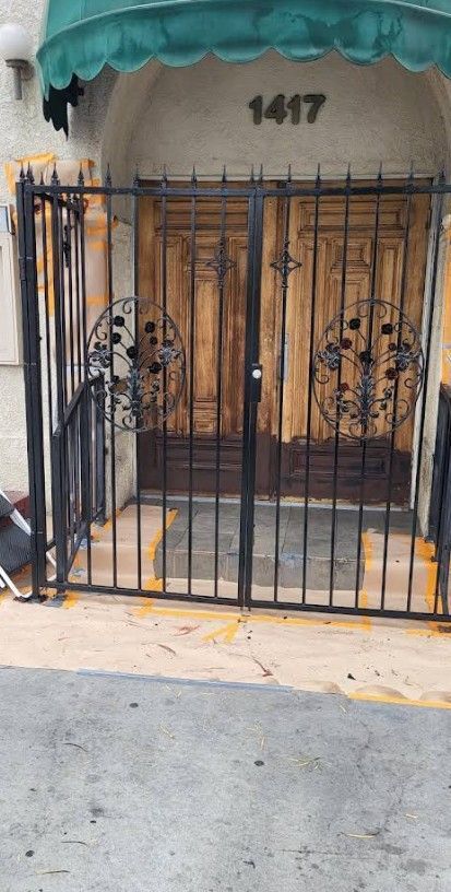 Black wrought iron gate and door, with gold accents, in front of building entrance.