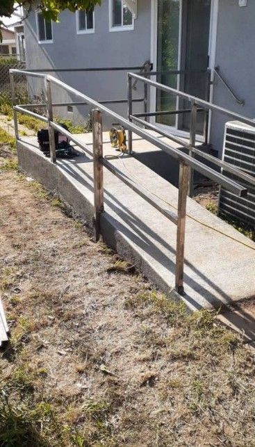 Concrete ramp with metal railings leading to a door; grass and building in background.
