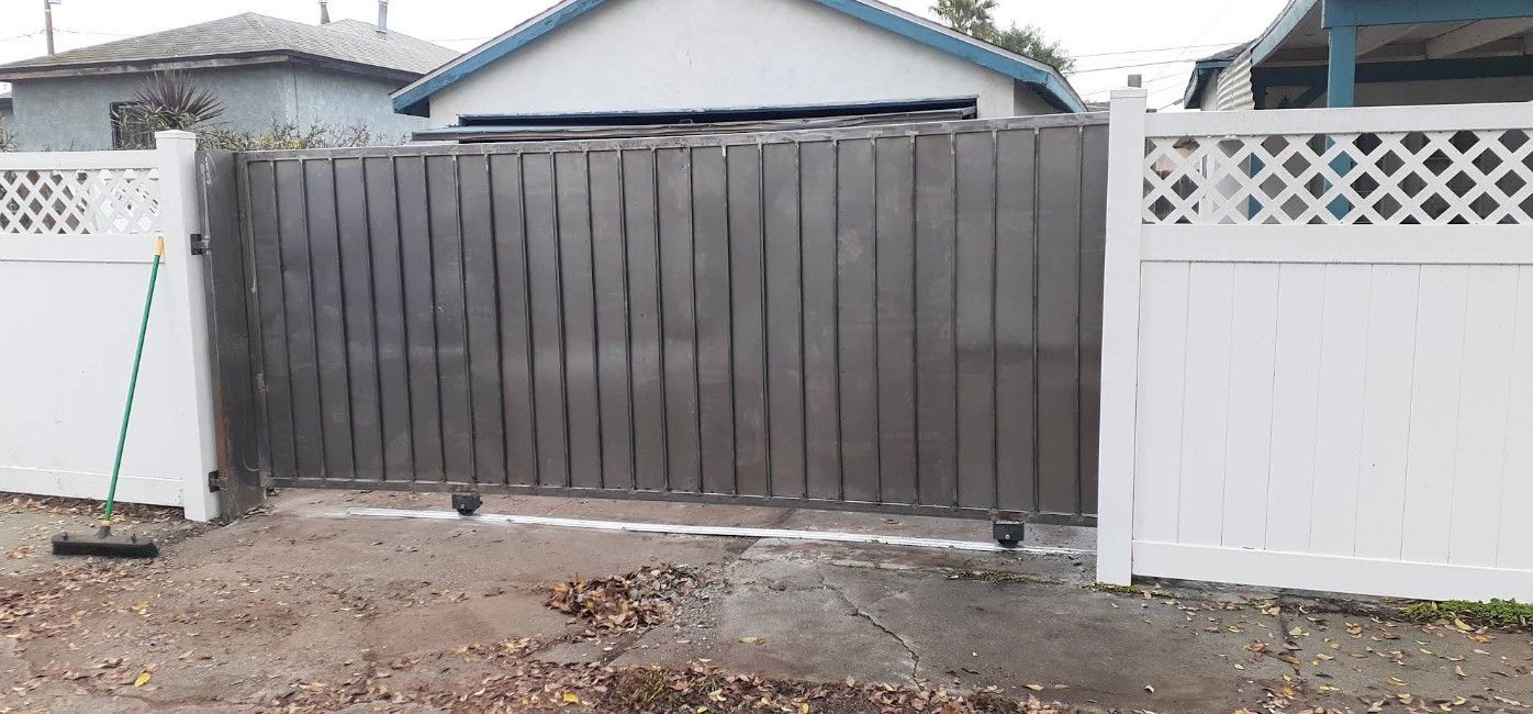 Gray wooden gate in a yard with a white fence on each side; a house is in the background.