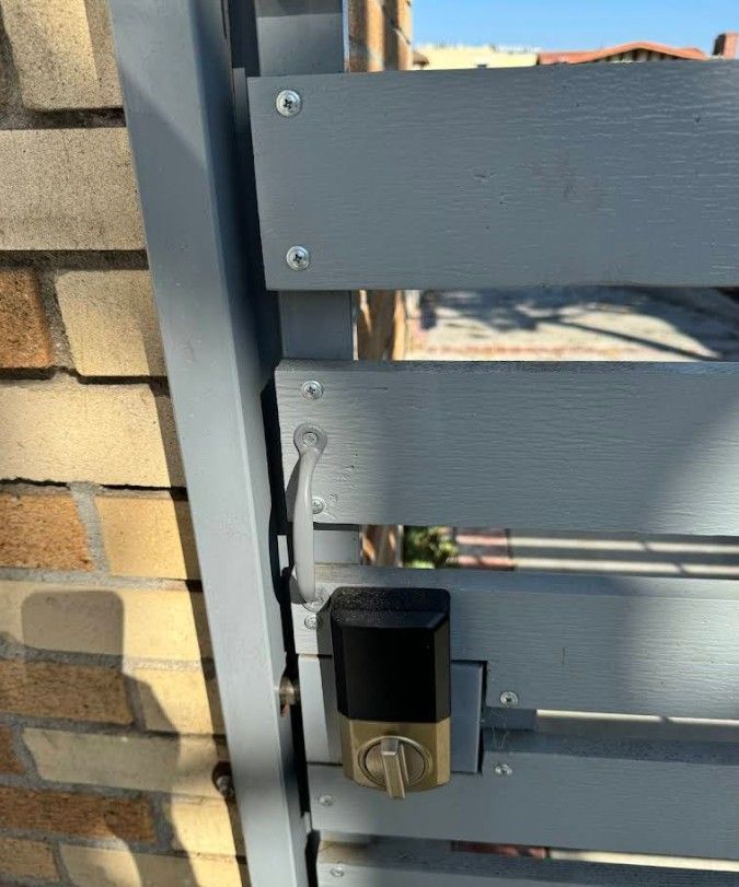 Gray metal gate with a smart lock and latch, attached to a brick wall.