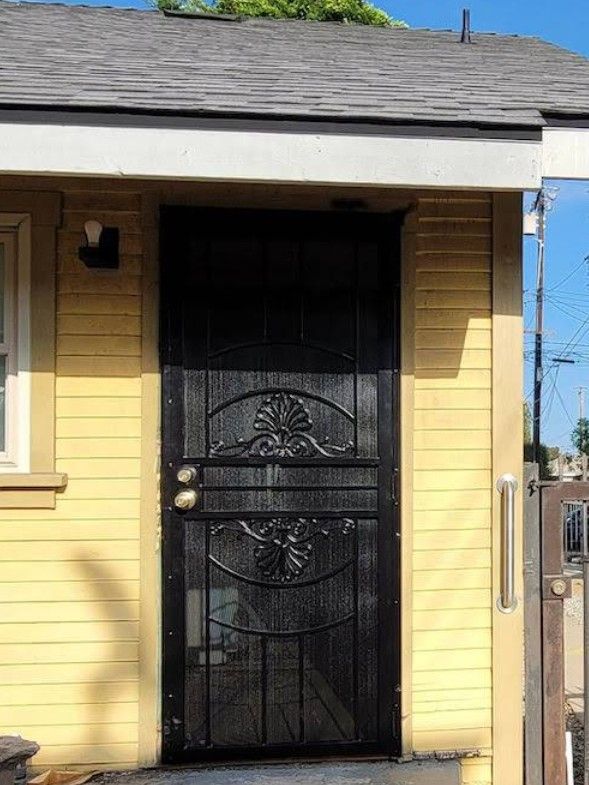 Black security door on a yellow building exterior with decorative floral design.