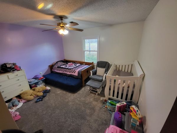 A bedroom with a bed , crib , dresser and ceiling fan.