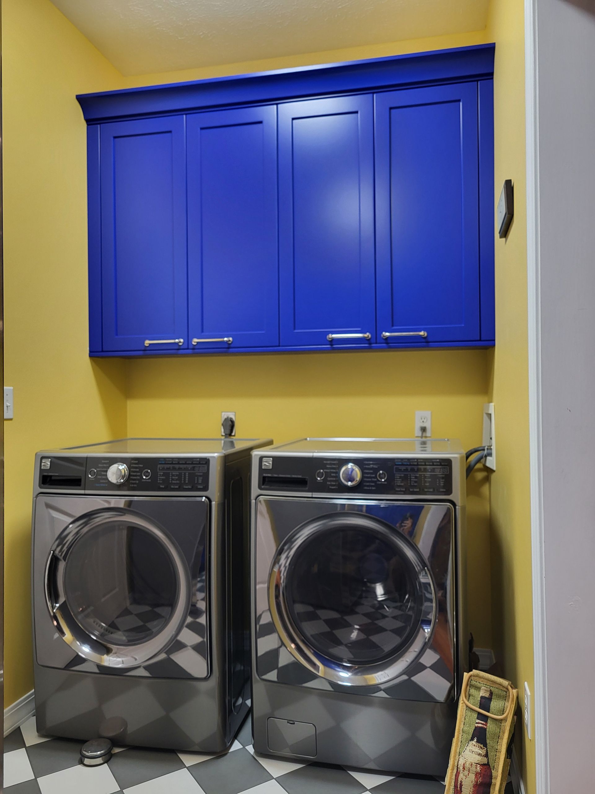 Two washers and dryers in a laundry room with blue cabinets