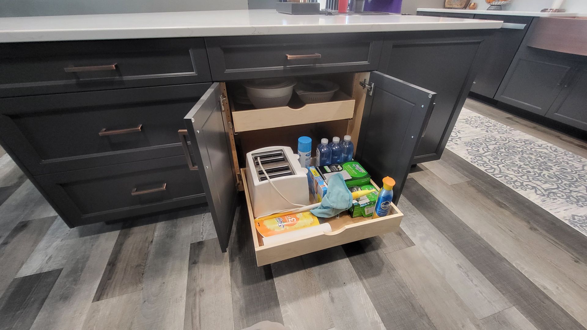 A kitchen island with a pull out drawer filled with cleaning supplies.