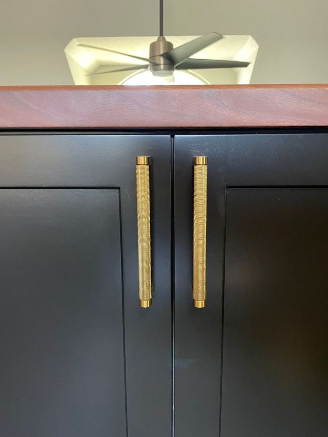 A black cabinet with gold handles and a ceiling fan above it