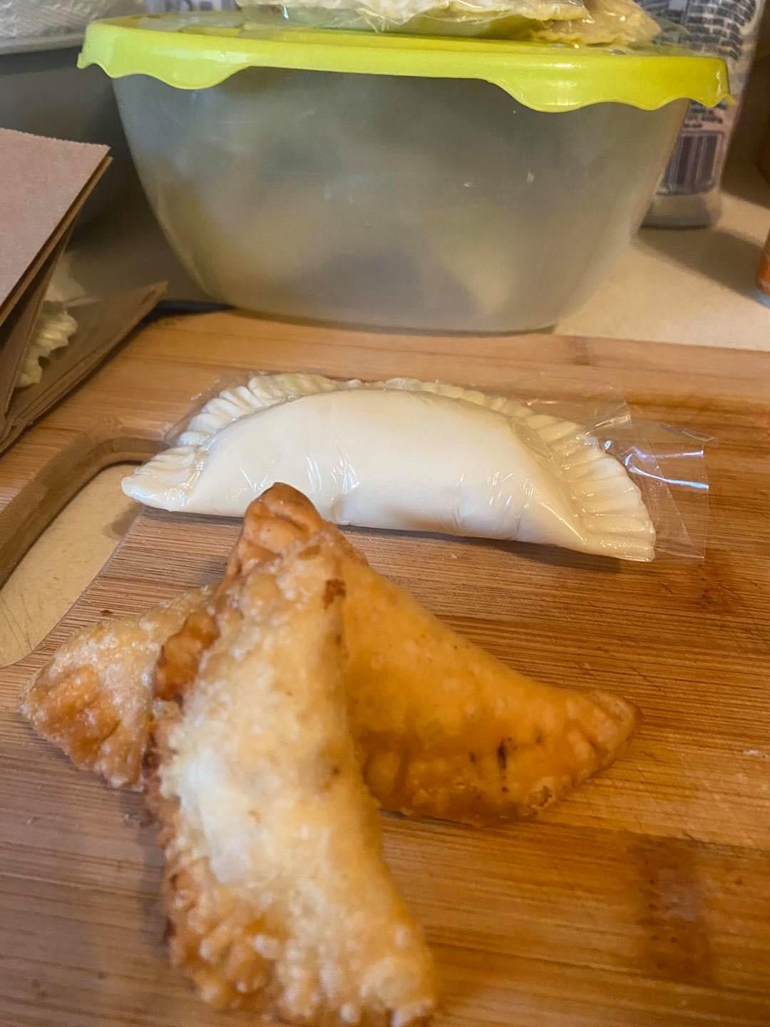 Fried and unfried empanadas on a wooden cutting board, with a bowl in the background.