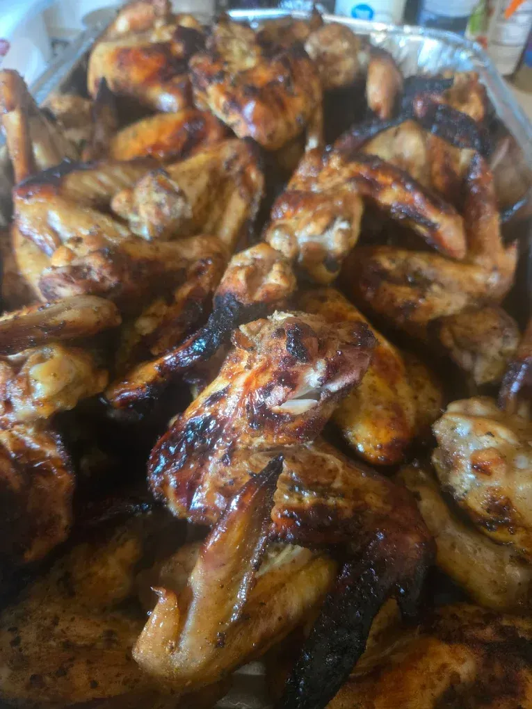 Pile of grilled chicken wings, golden brown with dark charred edges, in a metal tray.