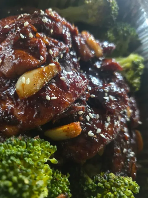 Chicken and broccoli dish, glistening dark sauce, sesame seeds, garlic cloves, broccoli florets.