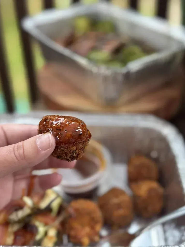 Person holding a fried food item, another tray with food in the background.