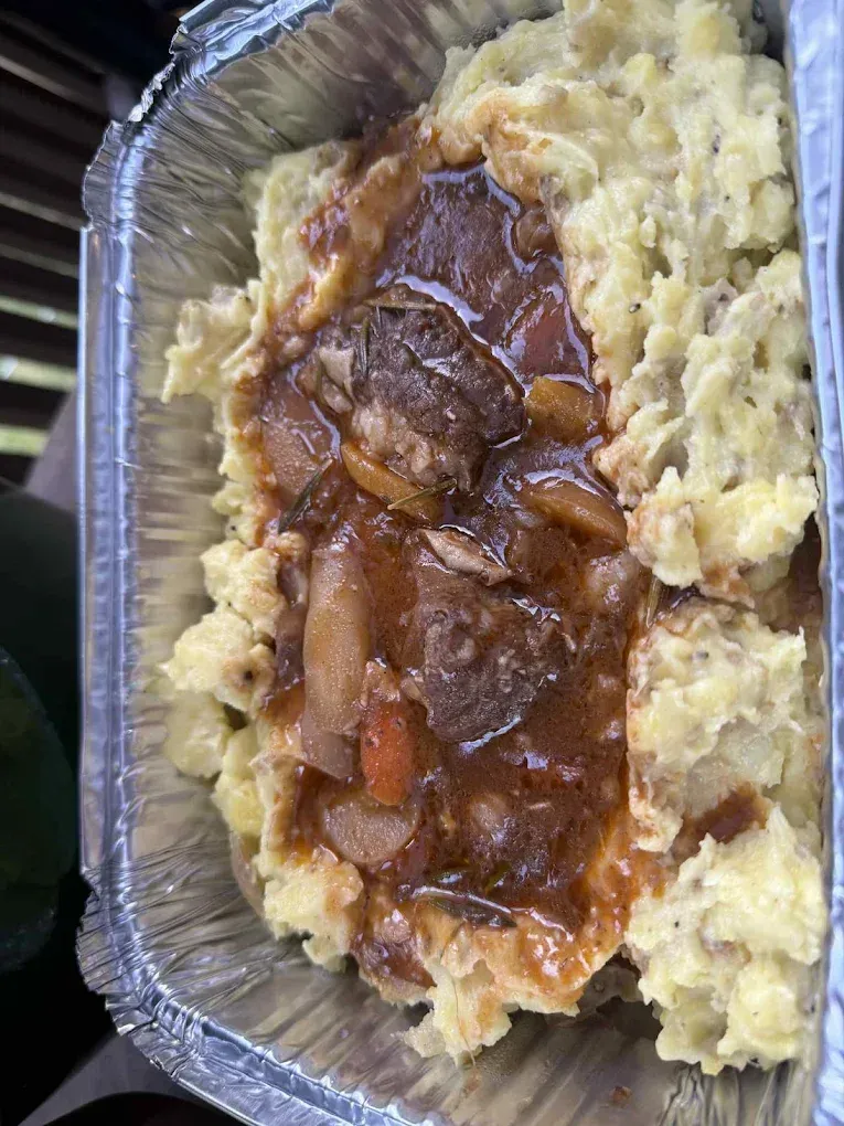 Beef stew with vegetables and gravy over mashed potatoes in a foil container.