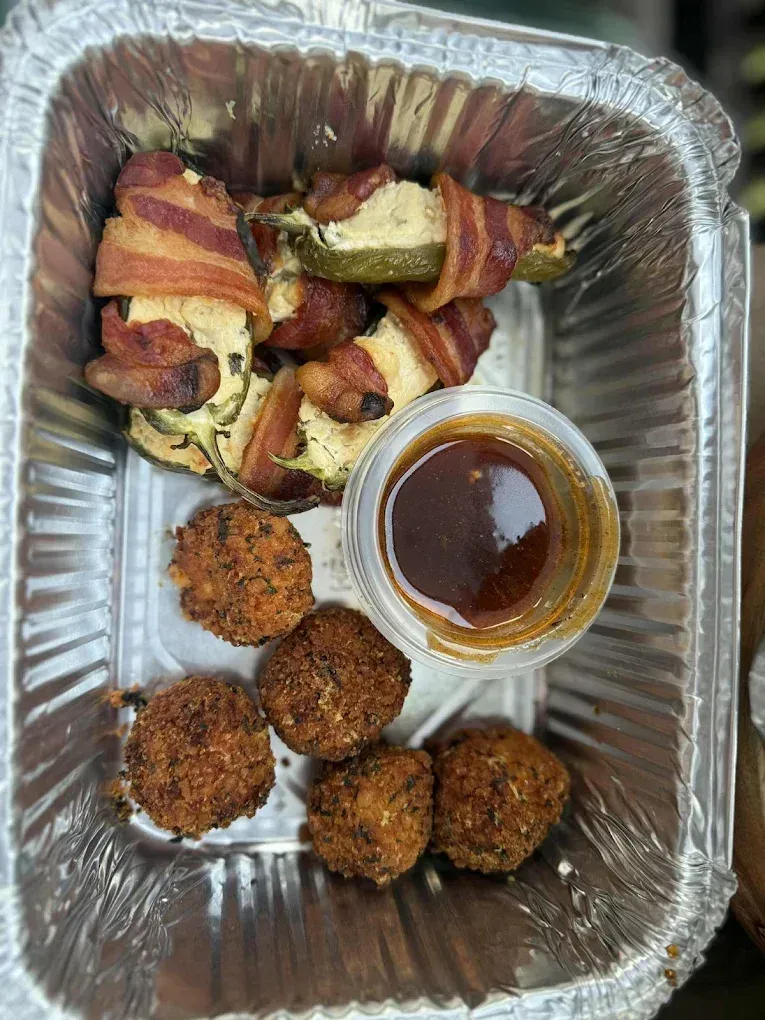 Tray of appetizers: bacon-wrapped jalapeños, fried balls, and a dipping sauce.