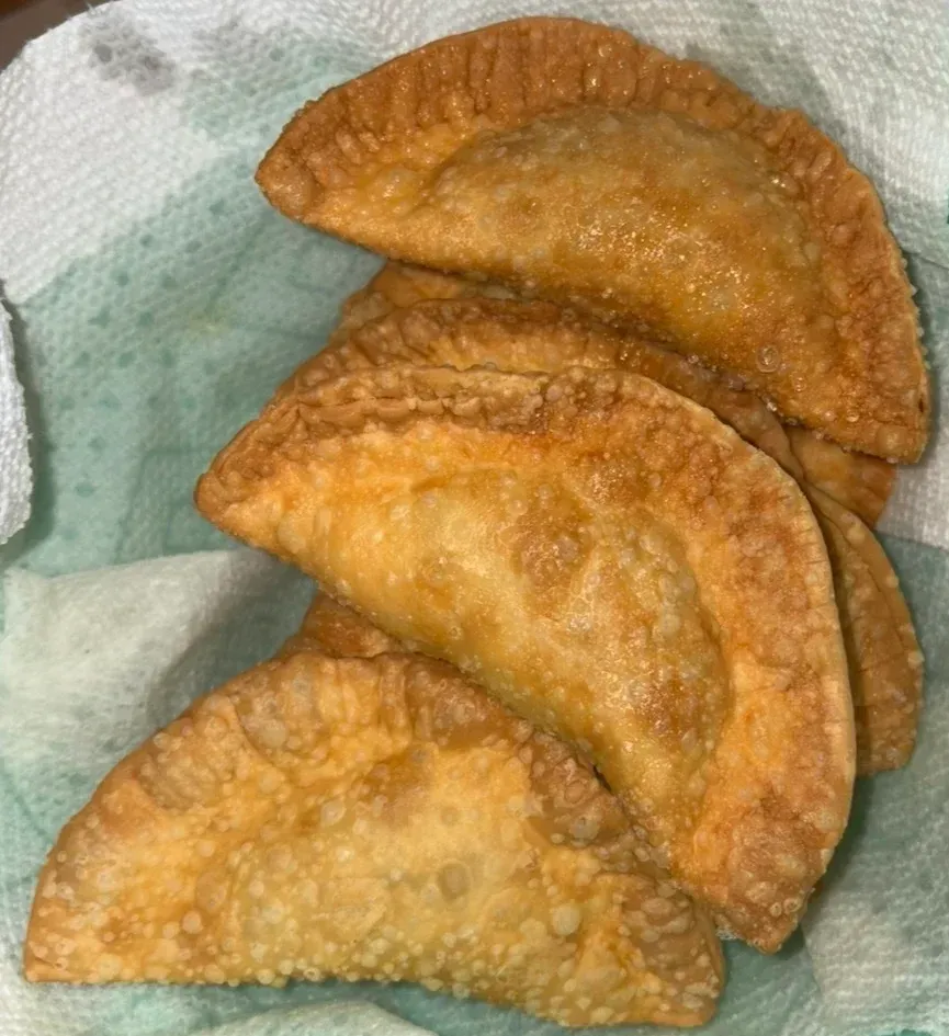 Pile of golden-brown fried empanadas on a paper towel.