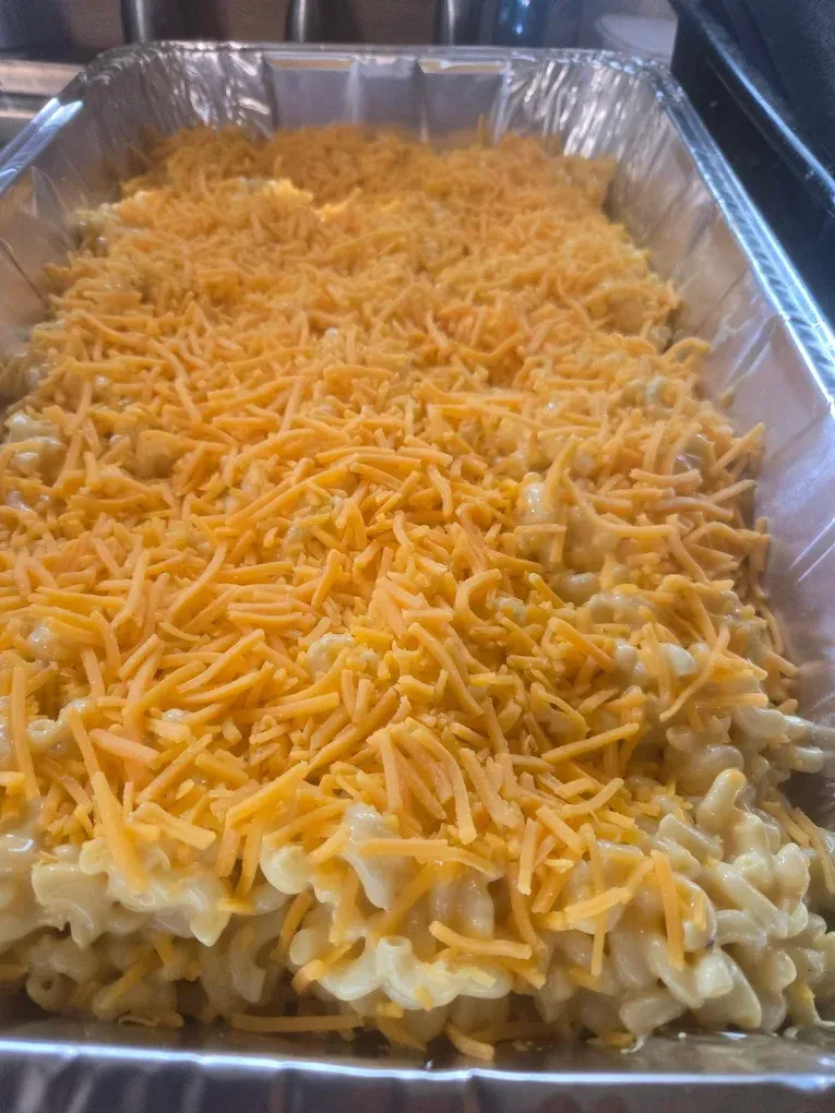 Mac and cheese in a rectangular aluminum pan, topped with shredded orange cheese.